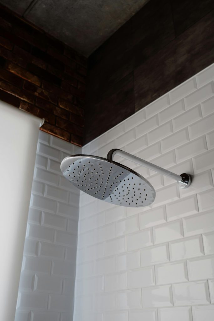 Sleek stainless steel shower head set against a stylish bathroom with white tiles and a brick accent wall.
